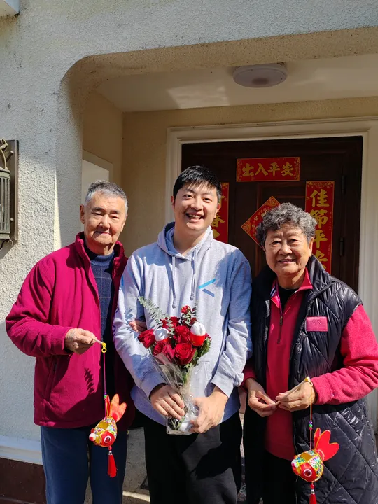 Jacky standing with family outdoors, holding flowers